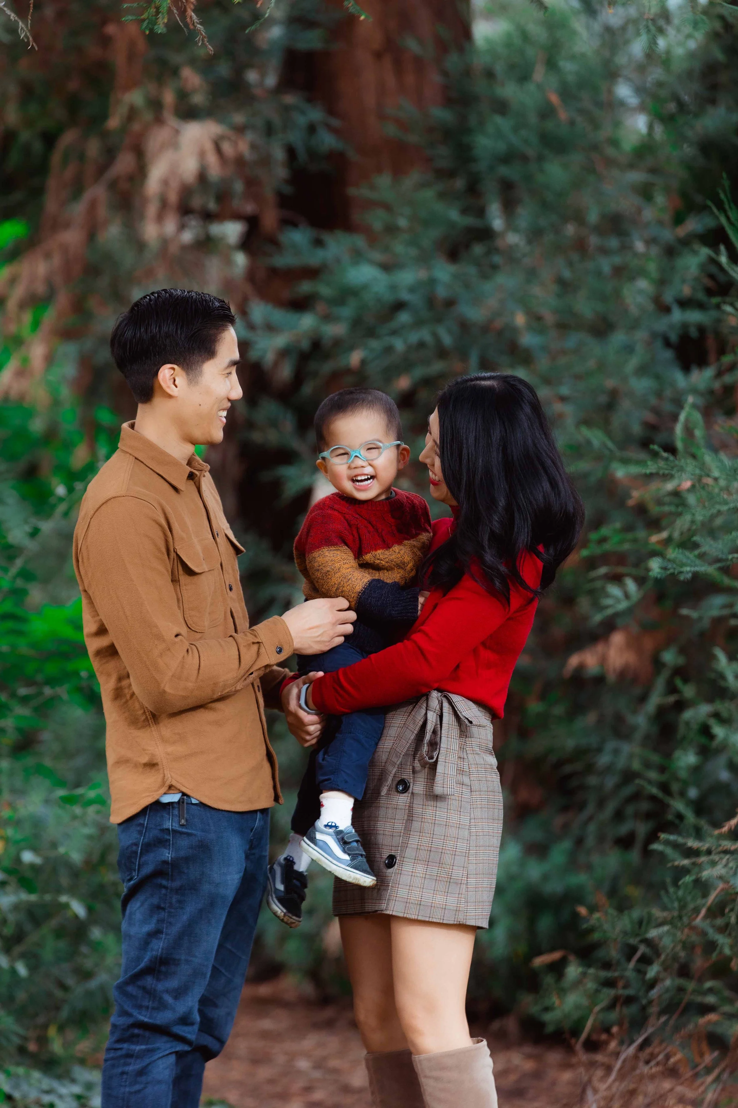 A family of three, a man, woman, and young boy, happily enjoying time outdoors among greenery and trees.