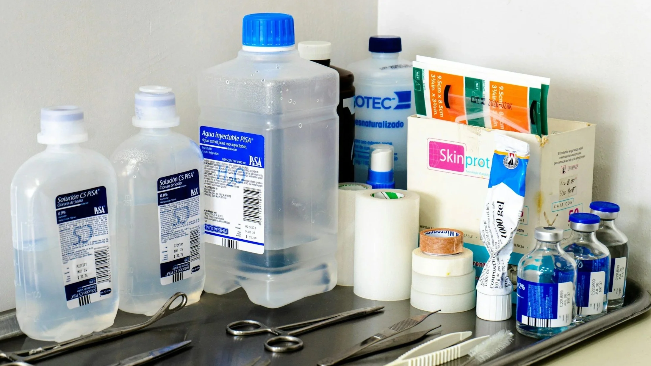 Medical supplies including bottles of disinfectant, adhesive tape rolls, scissors, forceps, and bandages on a hospital tray