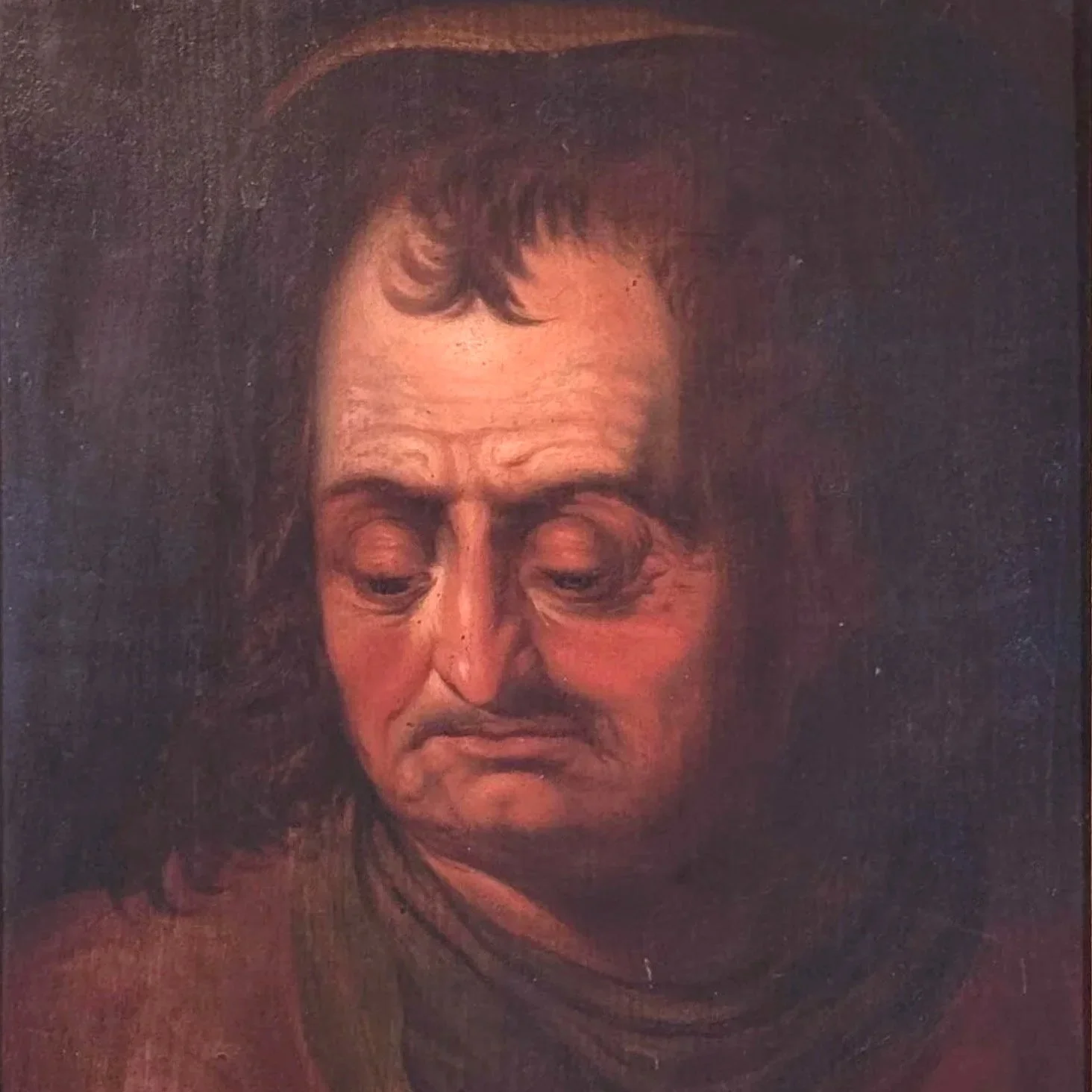 A person with long dark hair and a hat, looking down with a somber expression.