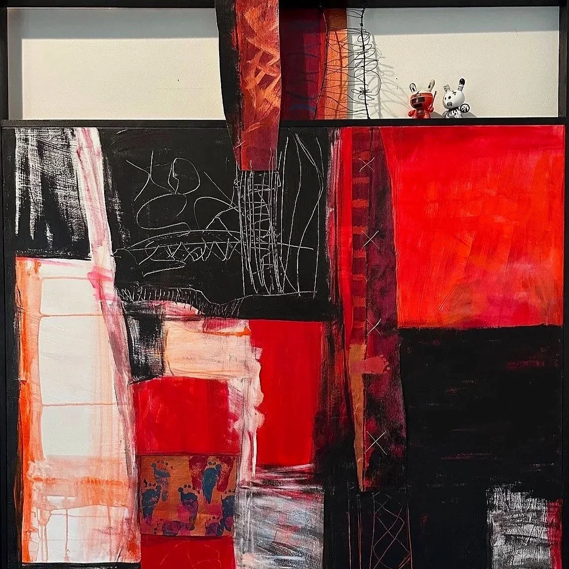 Abstract wall art with red, black, white, and orange sections, featuring scribbles, patterns, and two small animal figurines in the protected space at the top right corner.