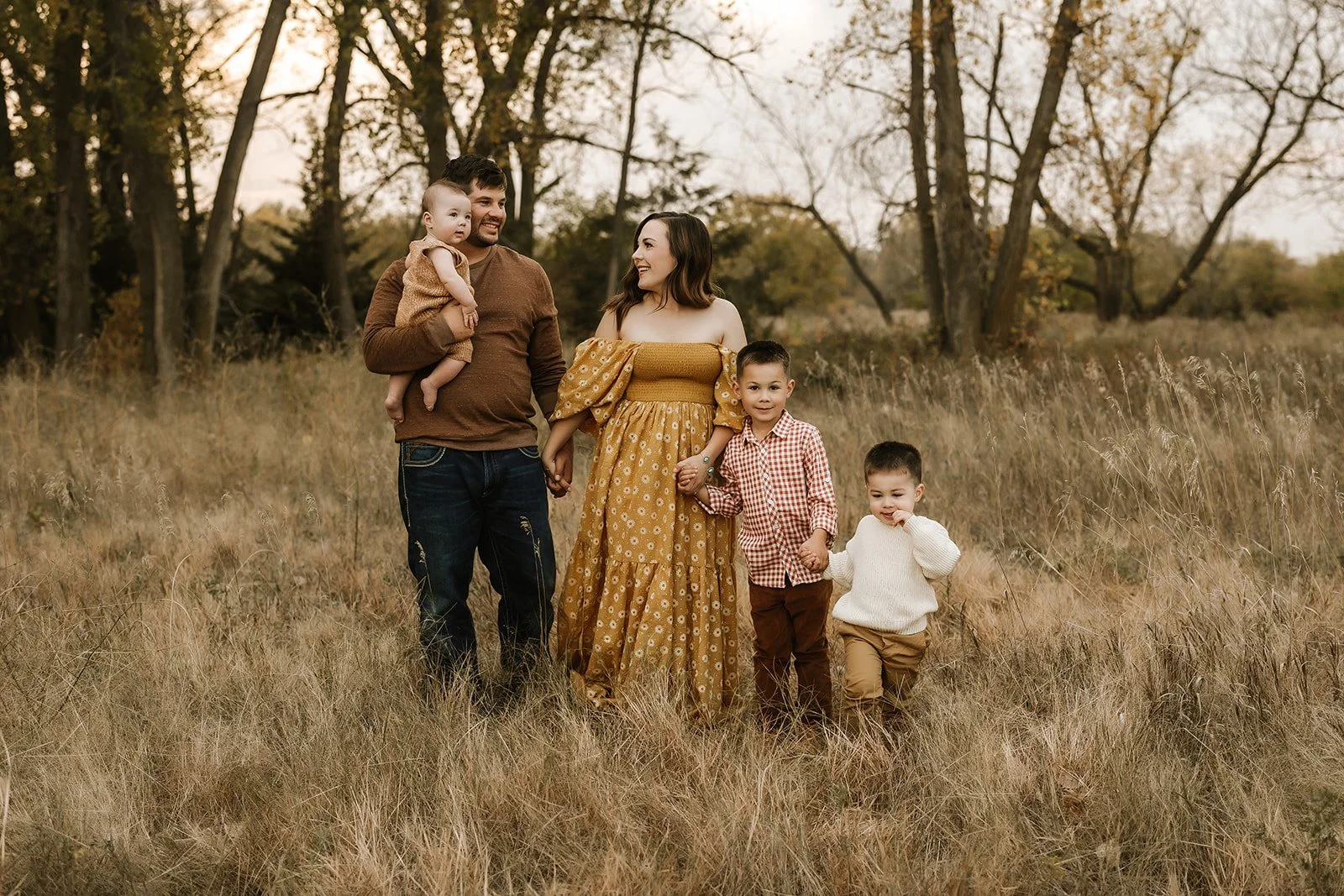 Kearney NE mom, dad and three young boys walk through a field styled for their family photos in fall colors