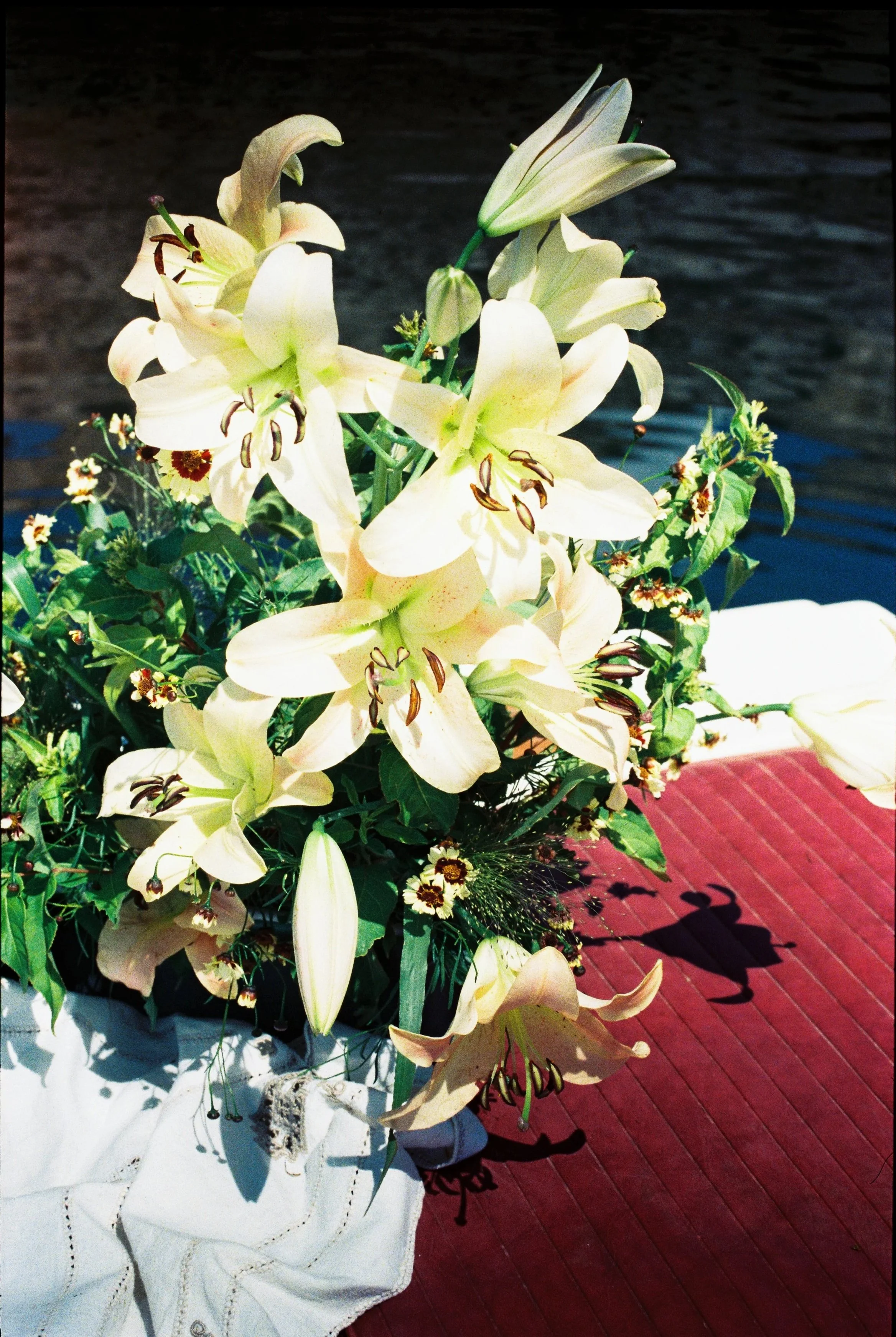 A bouquet of white lilies and small flowers placed on a red wooden surface.