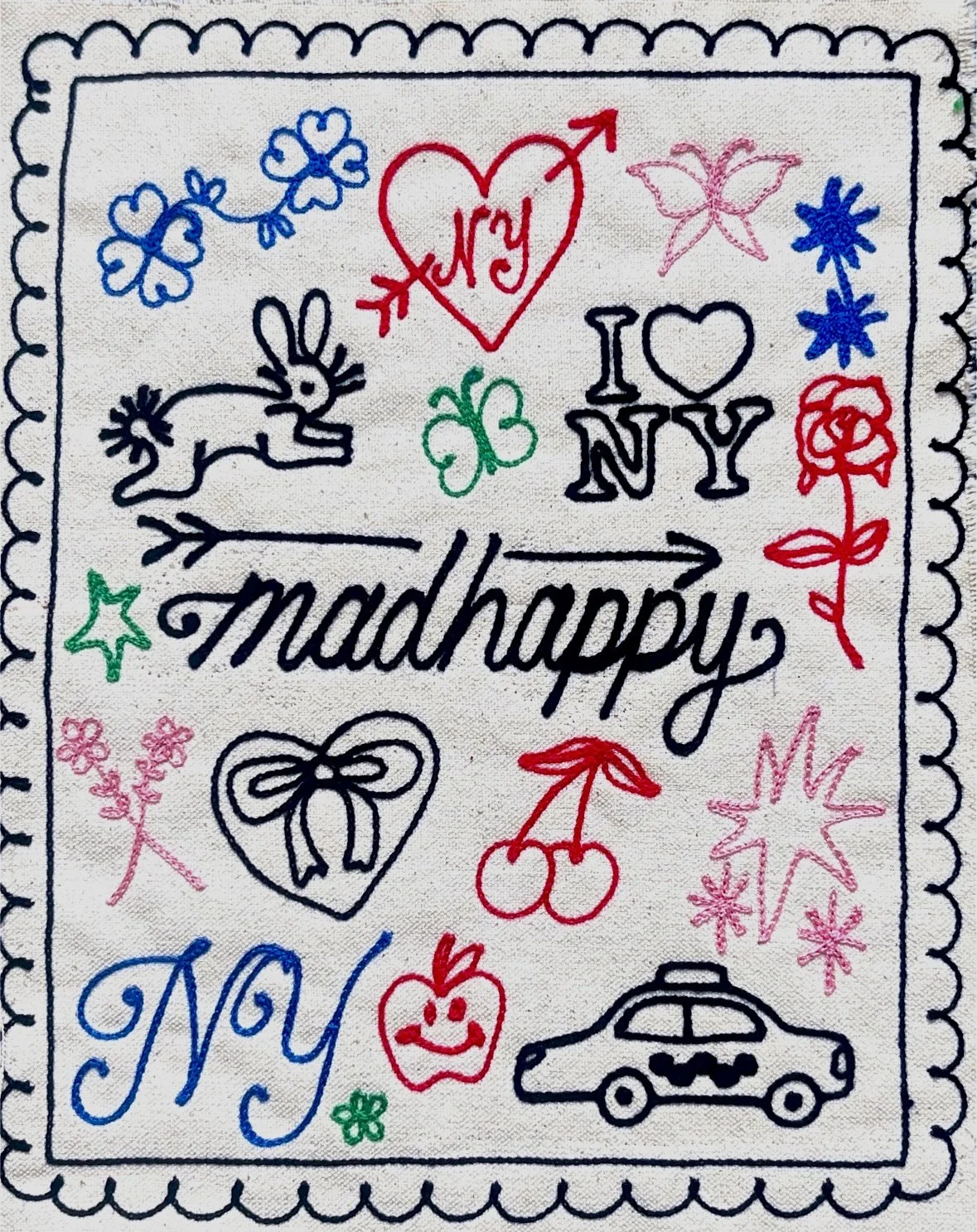 Colorful embroidered fabric with various doodles and text, including hearts, butterflies, flowers, a bunny, cherries, a smiley face, a car, and words like "madhappy" and "NYC."