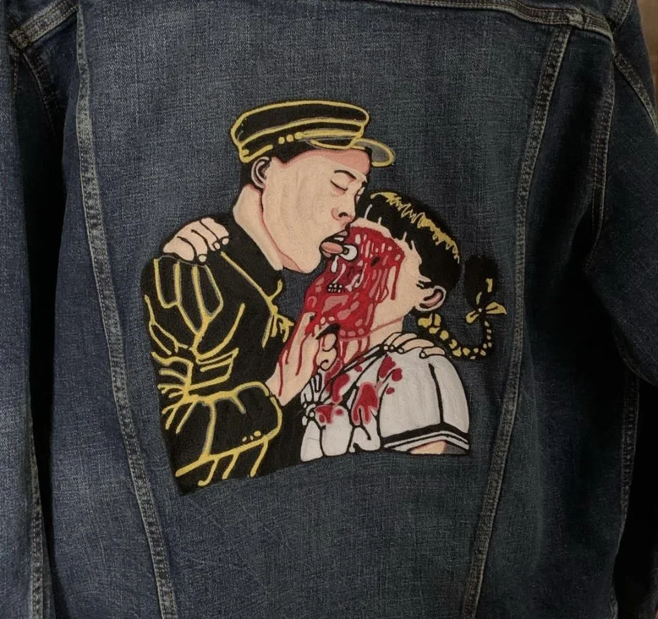 Patch on denim jacket showing a cartoon scene of a soldier licking a young girl with blood on her face.