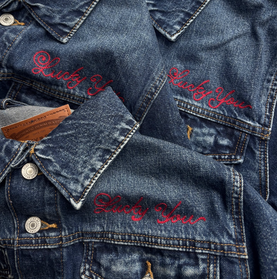 Close-up of denim jackets with red embroidered text that says 'Lucky You' on the chest area.