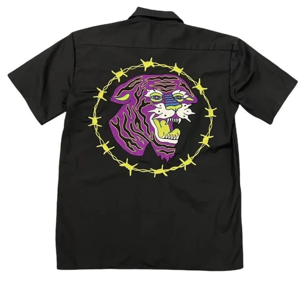 Black shirt with a colorful embroidered design of a tiger's head surrounded by yellow barbed wire.