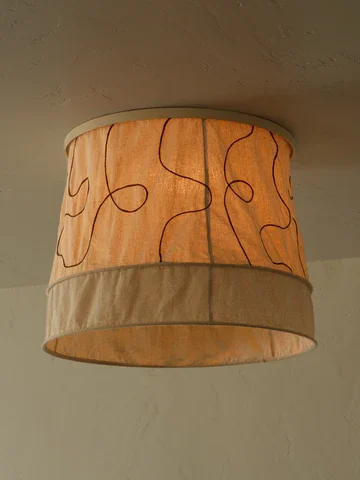 A ceiling-mounted lampshade with a beige fabric band and a cream-colored top, decorated with a pattern of black and red abstract squiggles.