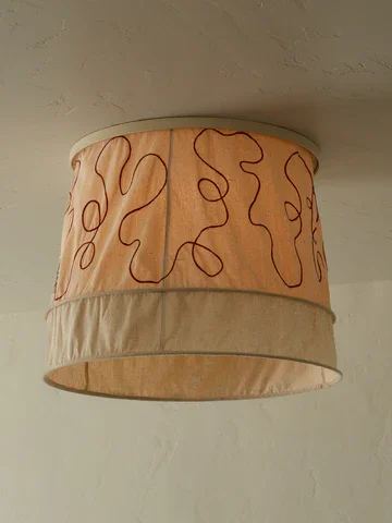 Ceiling light fixture with a beige fabric lampshade featuring red squiggly lines.