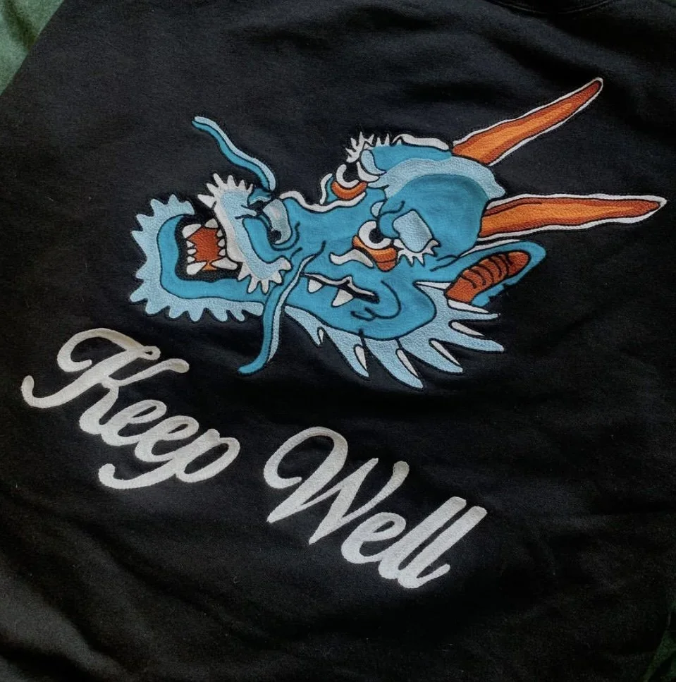 Graphic of a blue dragon with orange horns and claws, roaring with its mouth open, accompanied by the text "Keep Well" in cursive white font.