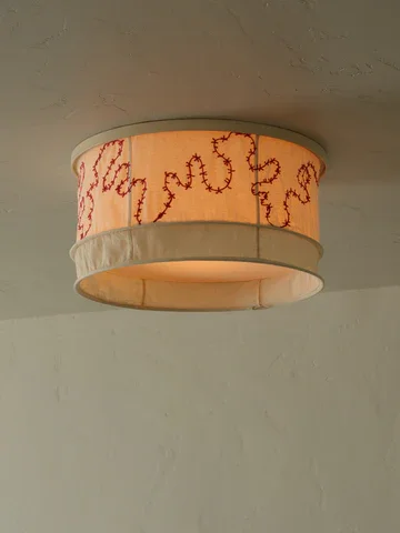 A ceiling light fixture with a cylindrical white shade featuring red handwritten text.