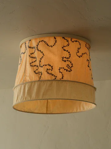 Ceiling-mounted beige lampshade with black embroidered squiggly lines and a darker beige band around the bottom edge.