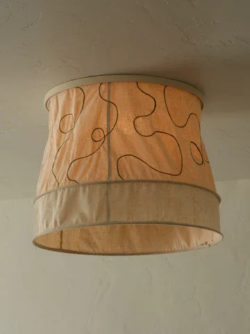 A ceiling lampshade with a beige fabric cover featuring black and orange squiggly lines.