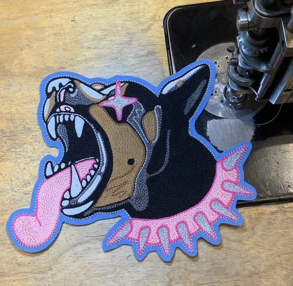 A patch of a snarling dog with star-shaped eye, sharp teeth, and tongue sticking out on a wooden surface near a sewing machine.