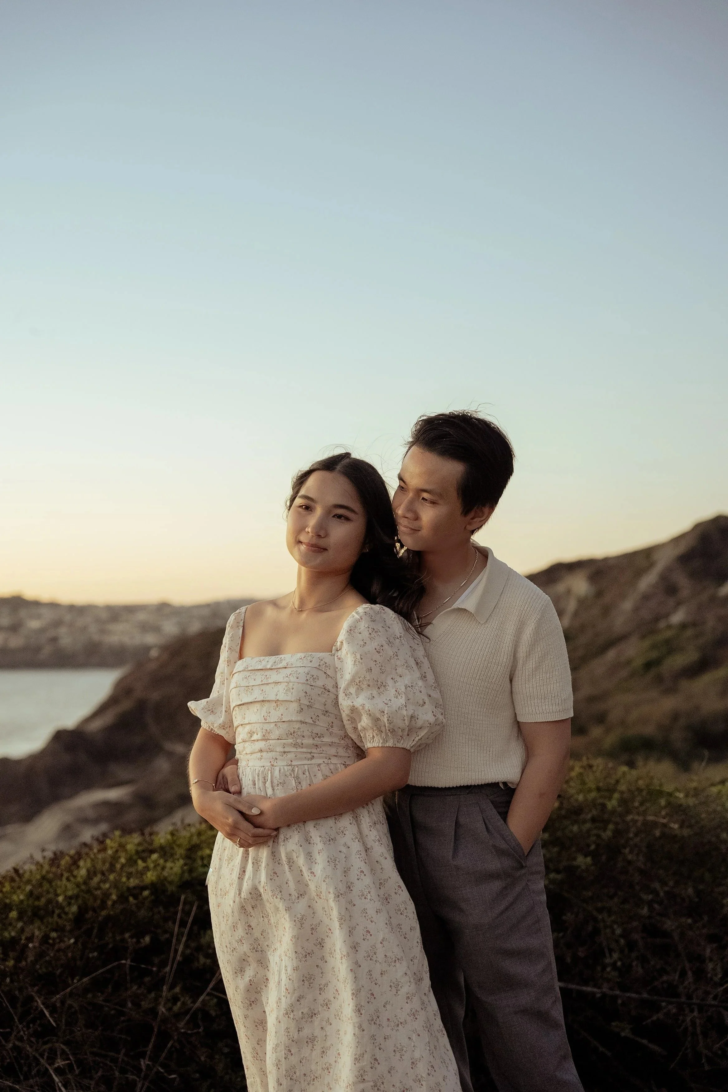 Sunset engagement photo of a couple at the Batteries to Bluff trail in San Francisco, standing on a hill next to the ocean