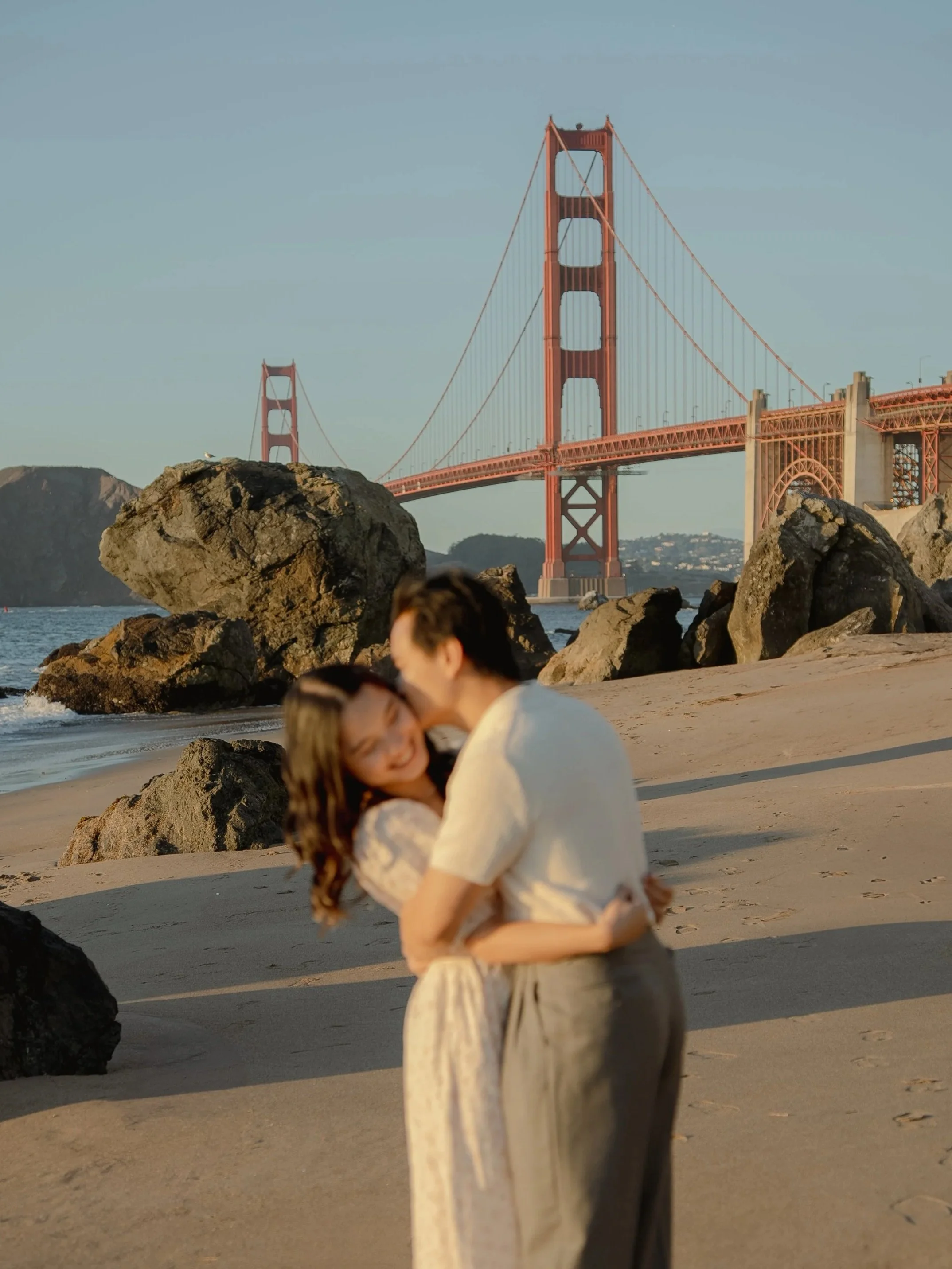 Engagement photo of a couple kissing at Marshall's Beach in San Francisco with the Golden Gate Bridge in the background.