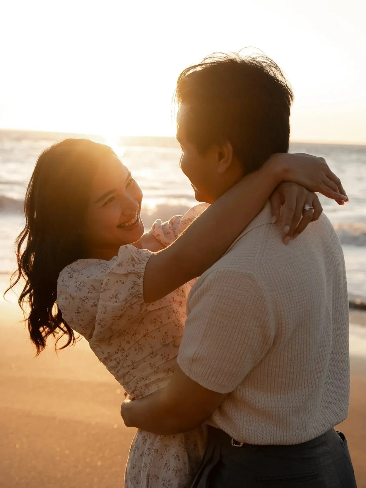 Engagement photo of a happy couple embraces at Marshall's Beach in San Francisco during sunset, smiling at each other.