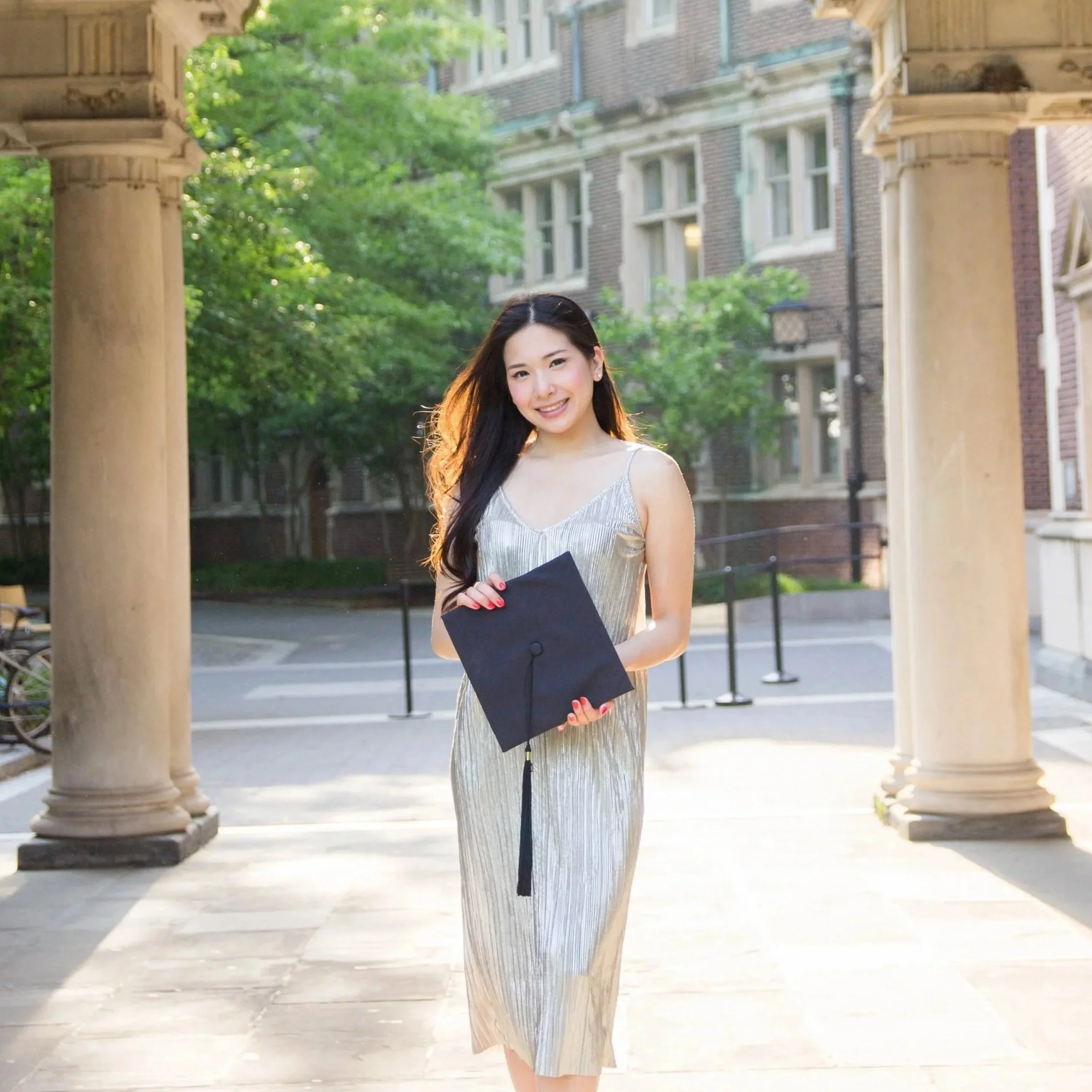 College senior portrait of an Asian woman holding a graduation cap at the University of Pennsylvania