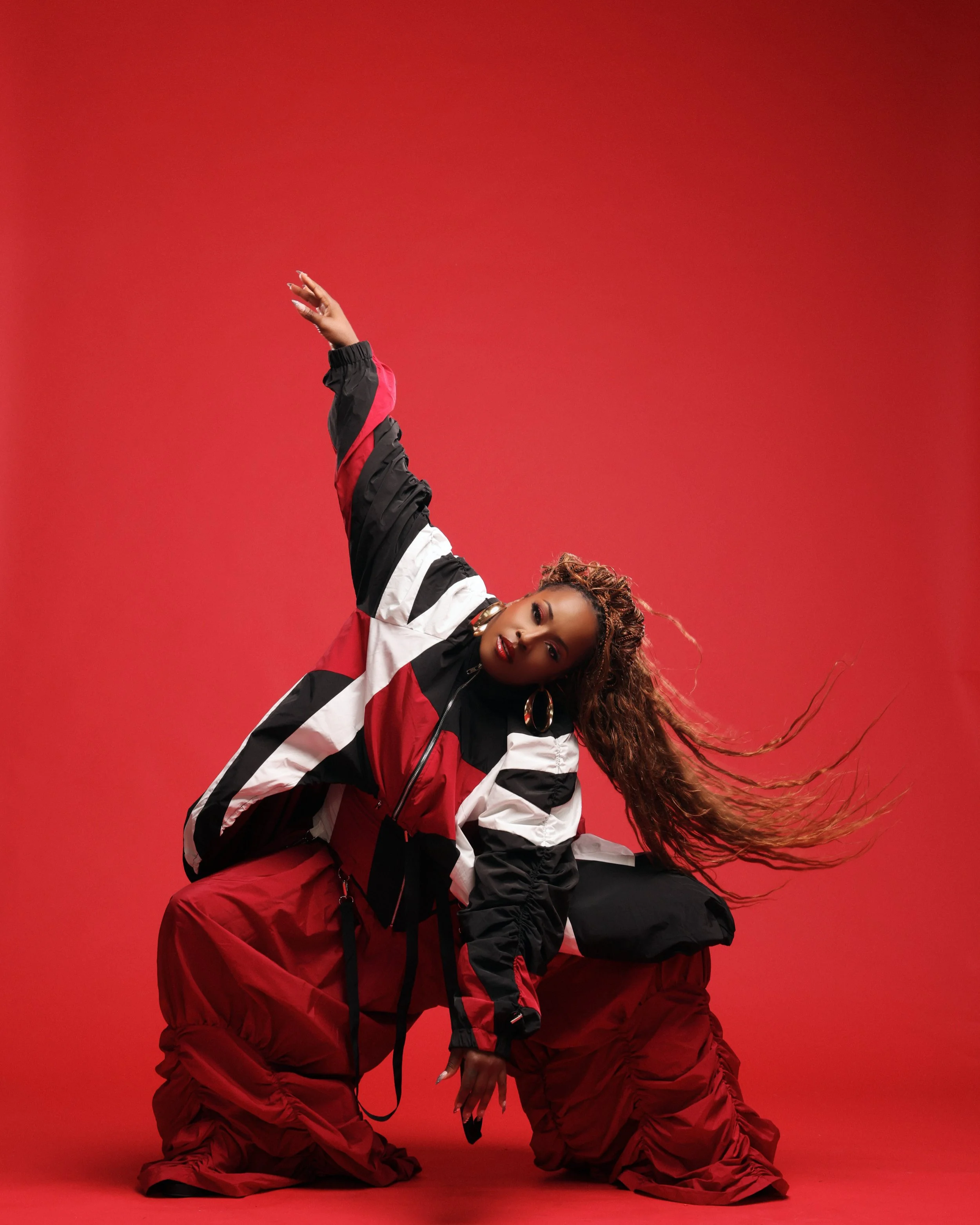 Miss Andye J posing in motion against a red studio backdrop.