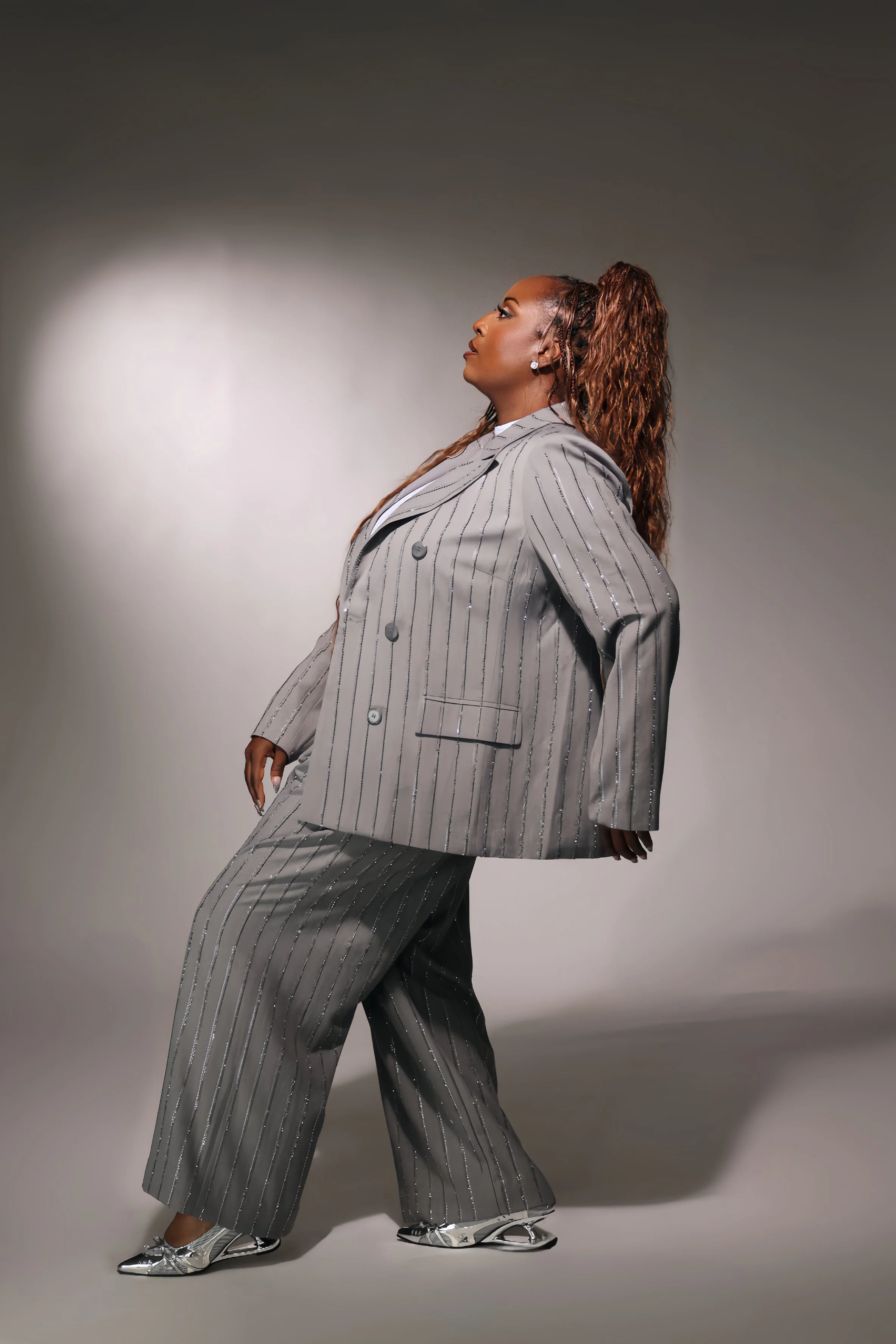 Andye J in a gray pinstriped suit, leaning back and looking upward in a creative studio portrait.