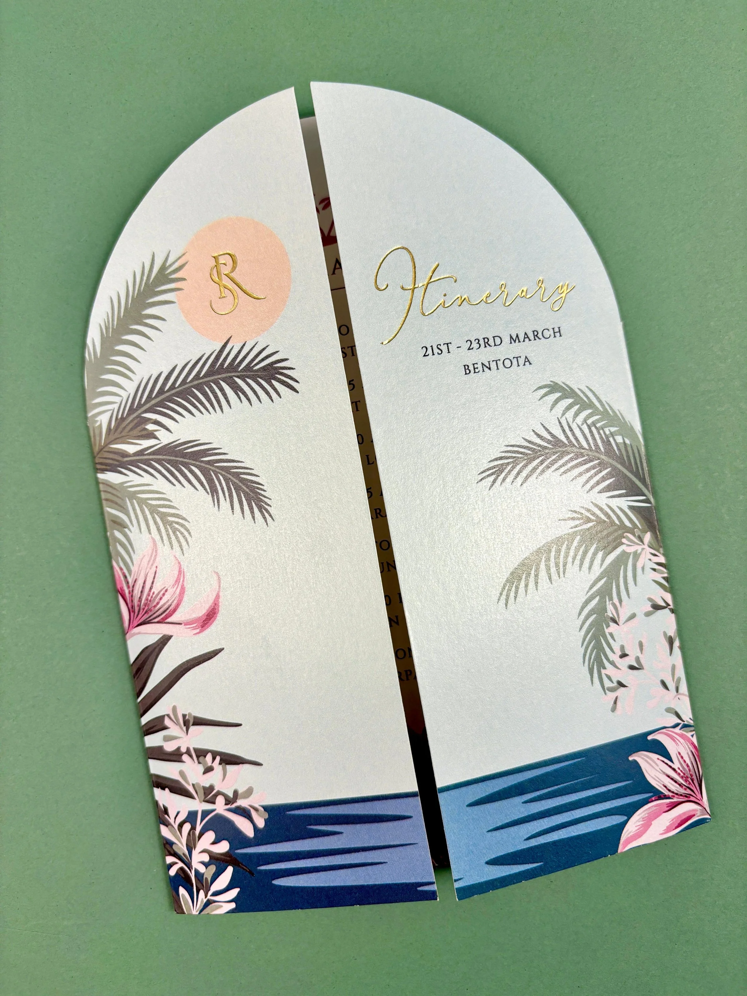 Split decorative itinerary card with palm trees and flowers, featuring gold lettering of 'Itinerary,' '21ST-23RD MARCH,' and 'BENTOTA' on a green background.