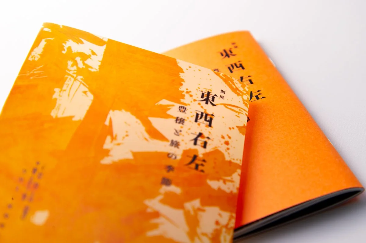 Orange brochure or pamphlet with black and white Japanese text and a stylized illustration of a tree and mountains on the cover.