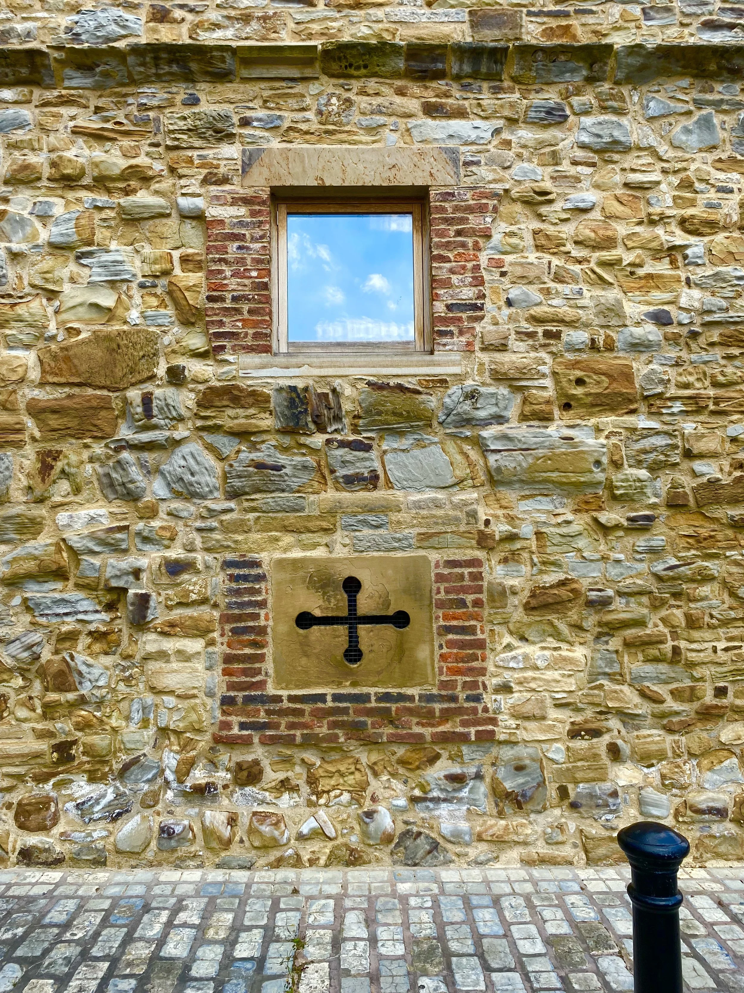 Small window set in a stone wall, reflecting sky and clouds