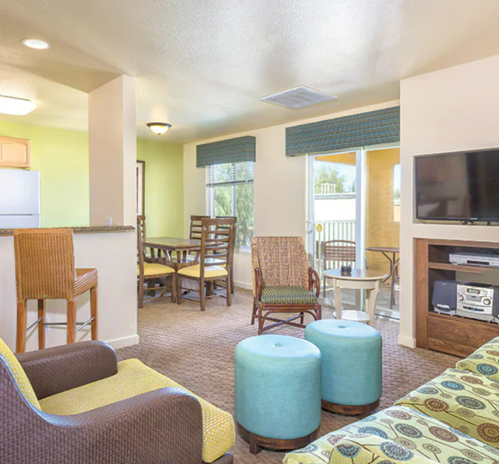 Living room with yellow, green, and patterned furniture, a dining area, and a sliding glass door leading to a balcony.