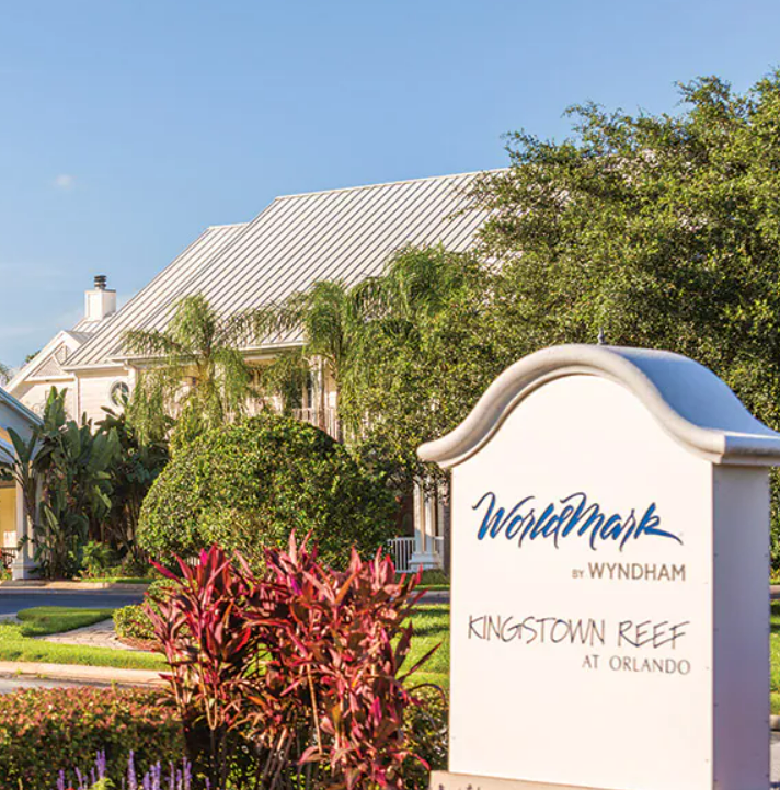 Sign for WorldMark by Wyndham at Kingstown Reef in Orlando, surrounded by tropical plants and trees outside a building with a metal roof.
