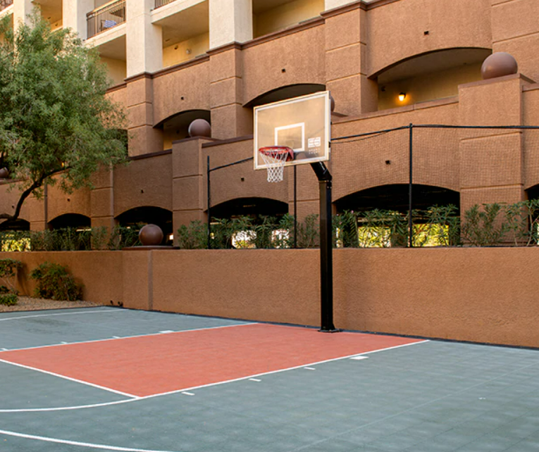 Outdoor basketball court with a backboard and hoop in front of a multi-story residential building.