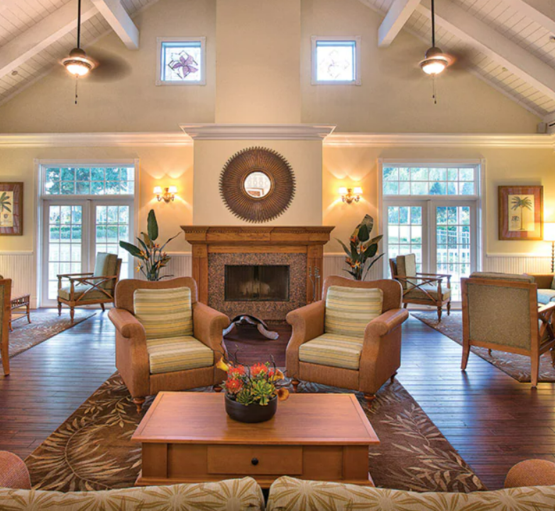 A cozy living room with a fireplace, comfortable chairs, large windows, and decorative artwork.