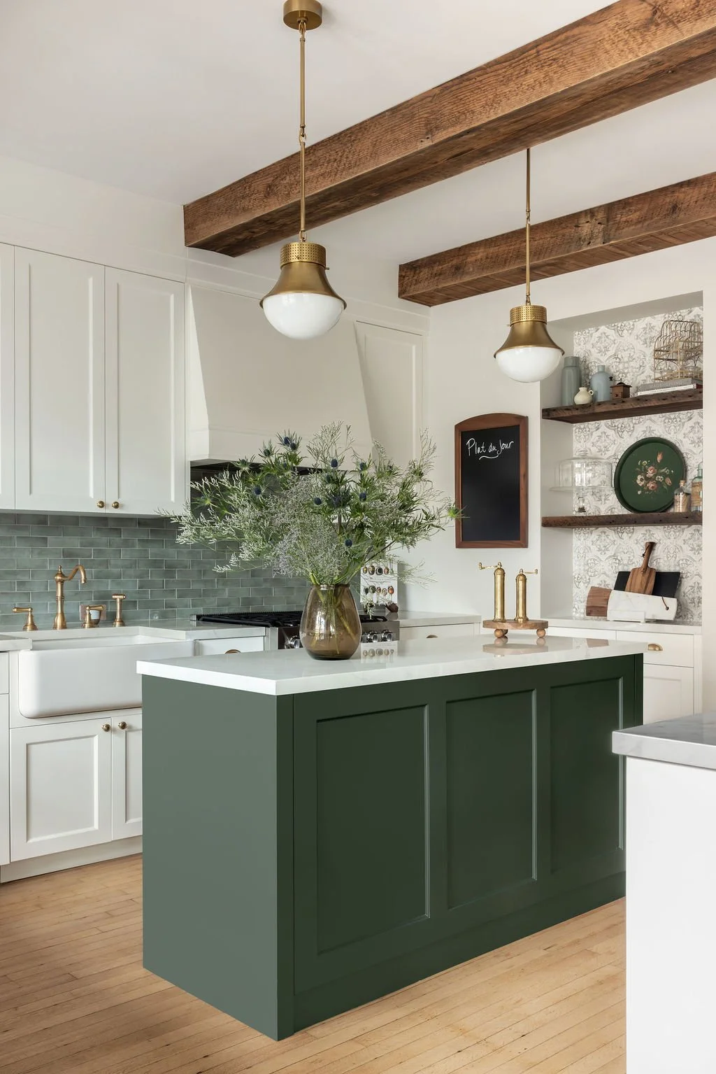 Modern kitchen with white cabinets, green island, wood beams on ceiling, pendant lights, and decorative shelves.