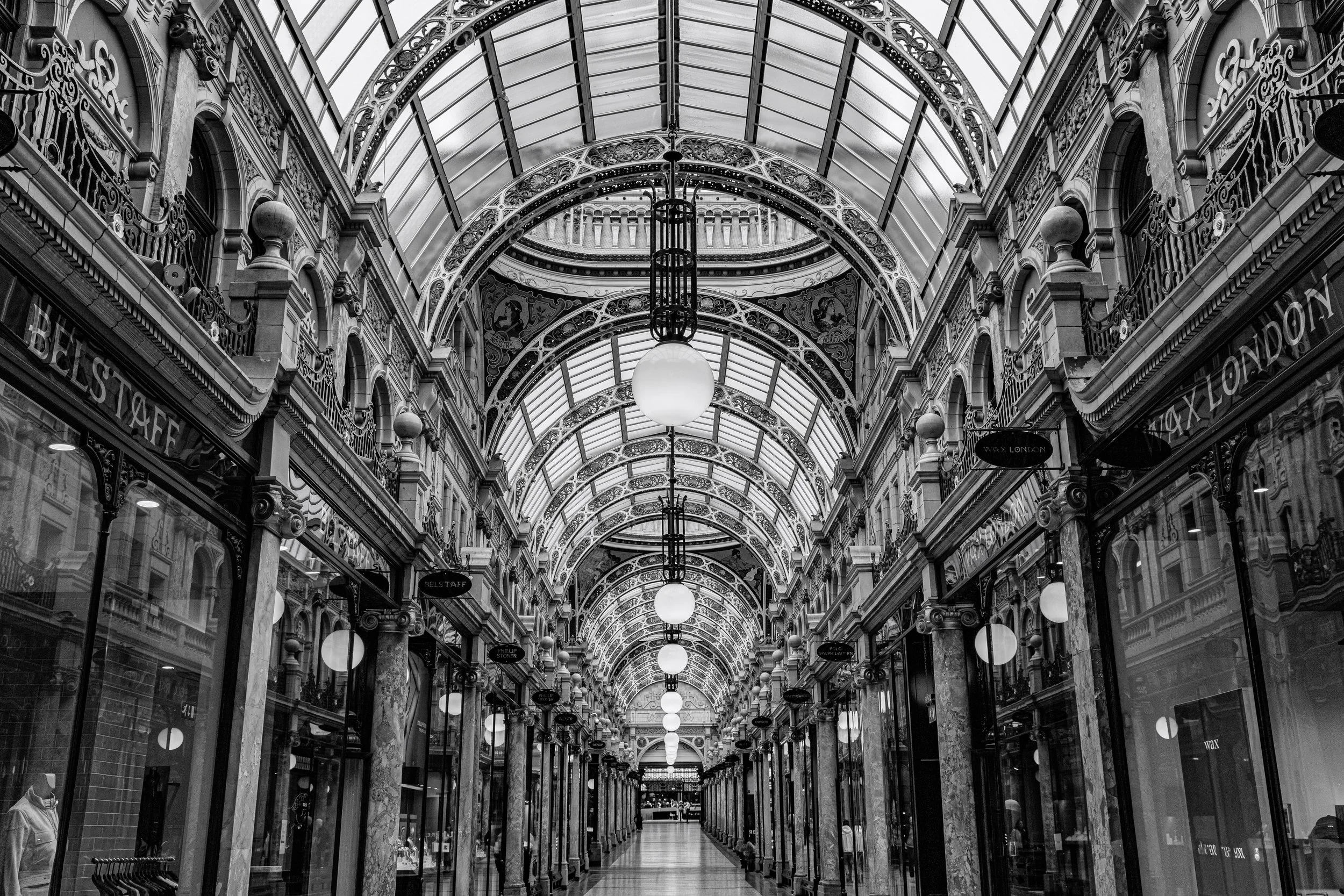 Black and white architectural photograph of the Victorian Quarter shopping arcade with glass roof, ironwork and strong perspective lines.