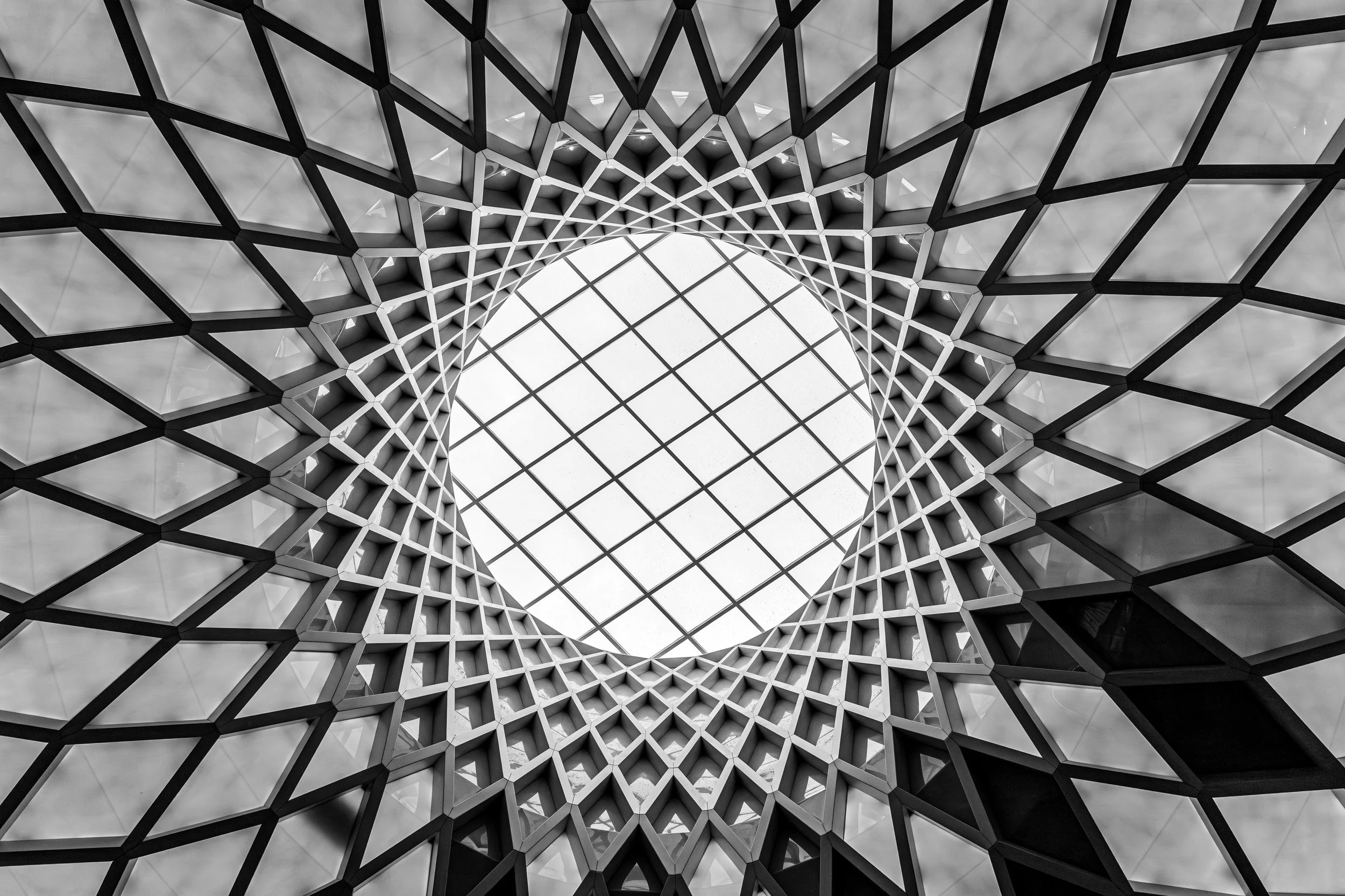 Black and white architectural photograph looking up at a circular ceiling structure with repeating geometric lines and bright central light.