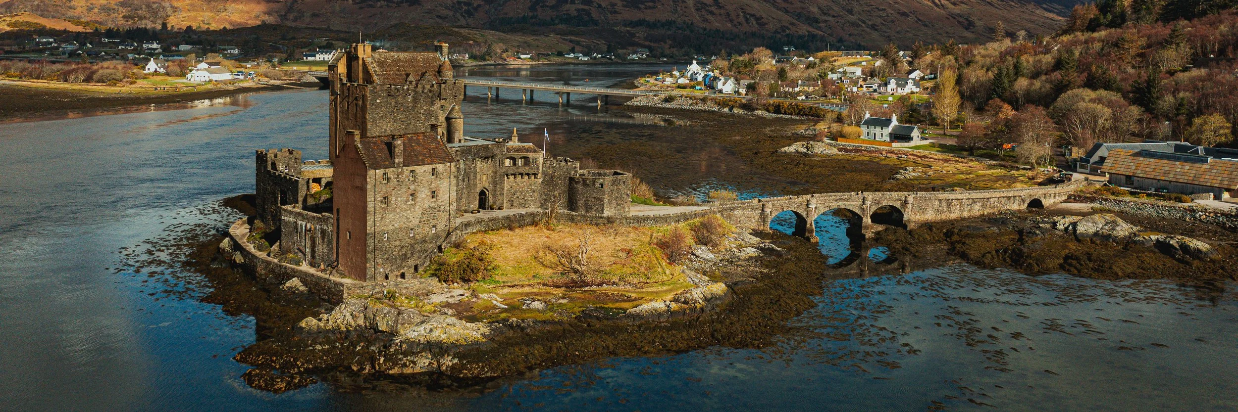 Close aerial panoramic view of Eilean Donan Castle in Scotland with stone bridge, water and Highland landscape.