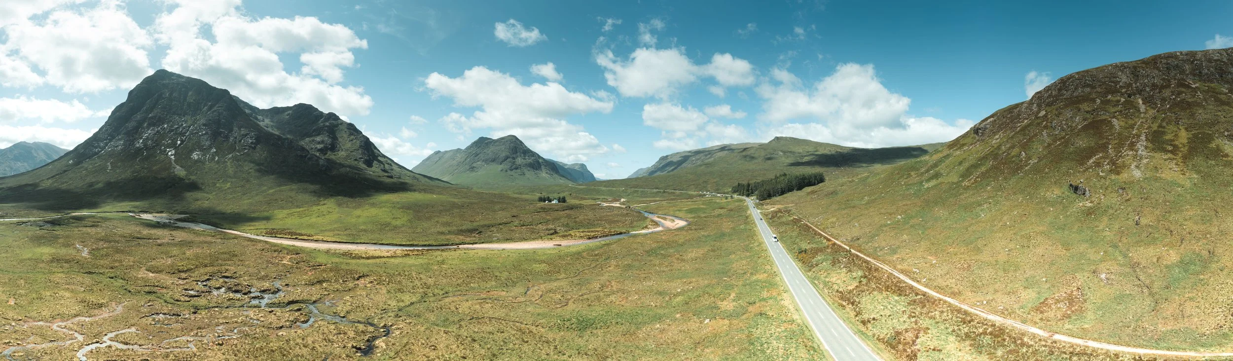 Wide aerial panorama of the Great Valley in Glencoe, Scotland, with road, green hills and mountains.