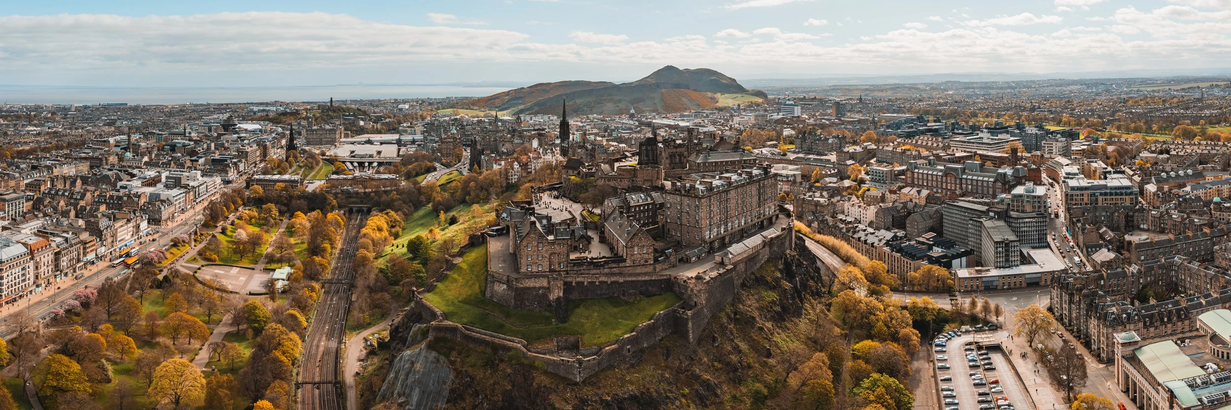Aerial panoramic view of Edinburgh Castle in Scotland with city buildings and Arthur’s Seat in the background.
