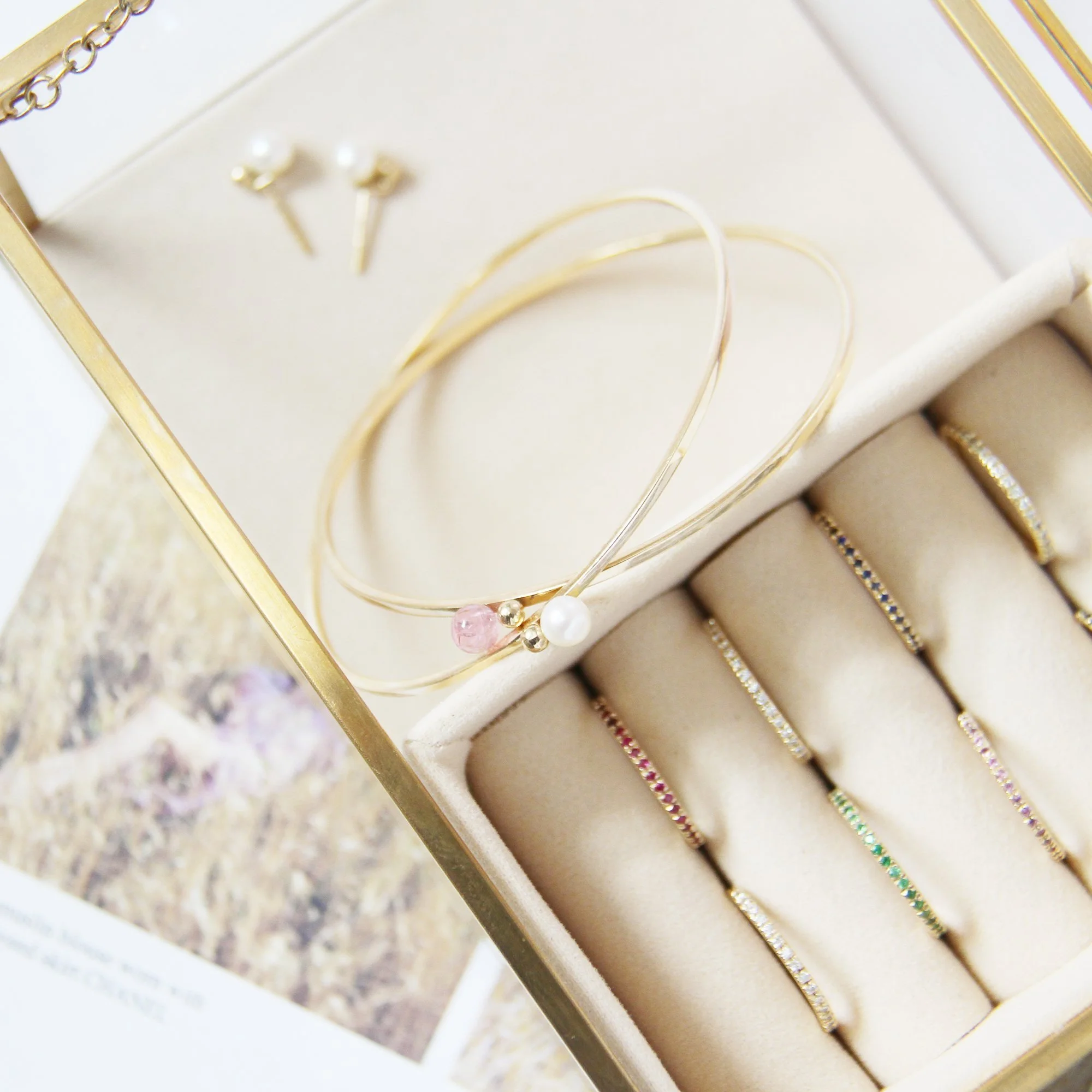 Glass, gold and cream velvet jewellery box, with gold eternity rings, bangles and pearl earrings.