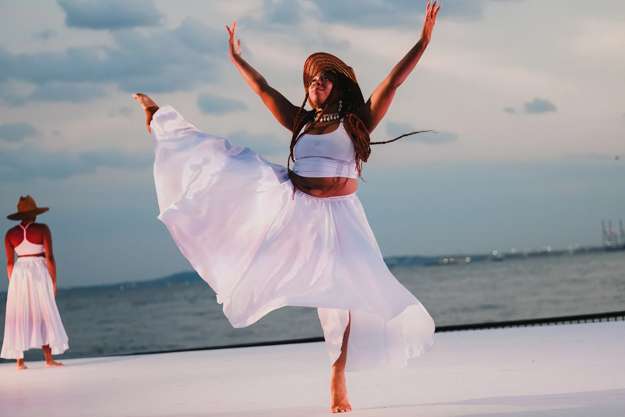NANM dancer in a white crop top and full white skirt at Robert F. Wagner Jr. Park, arms spread wide, skirt billowing