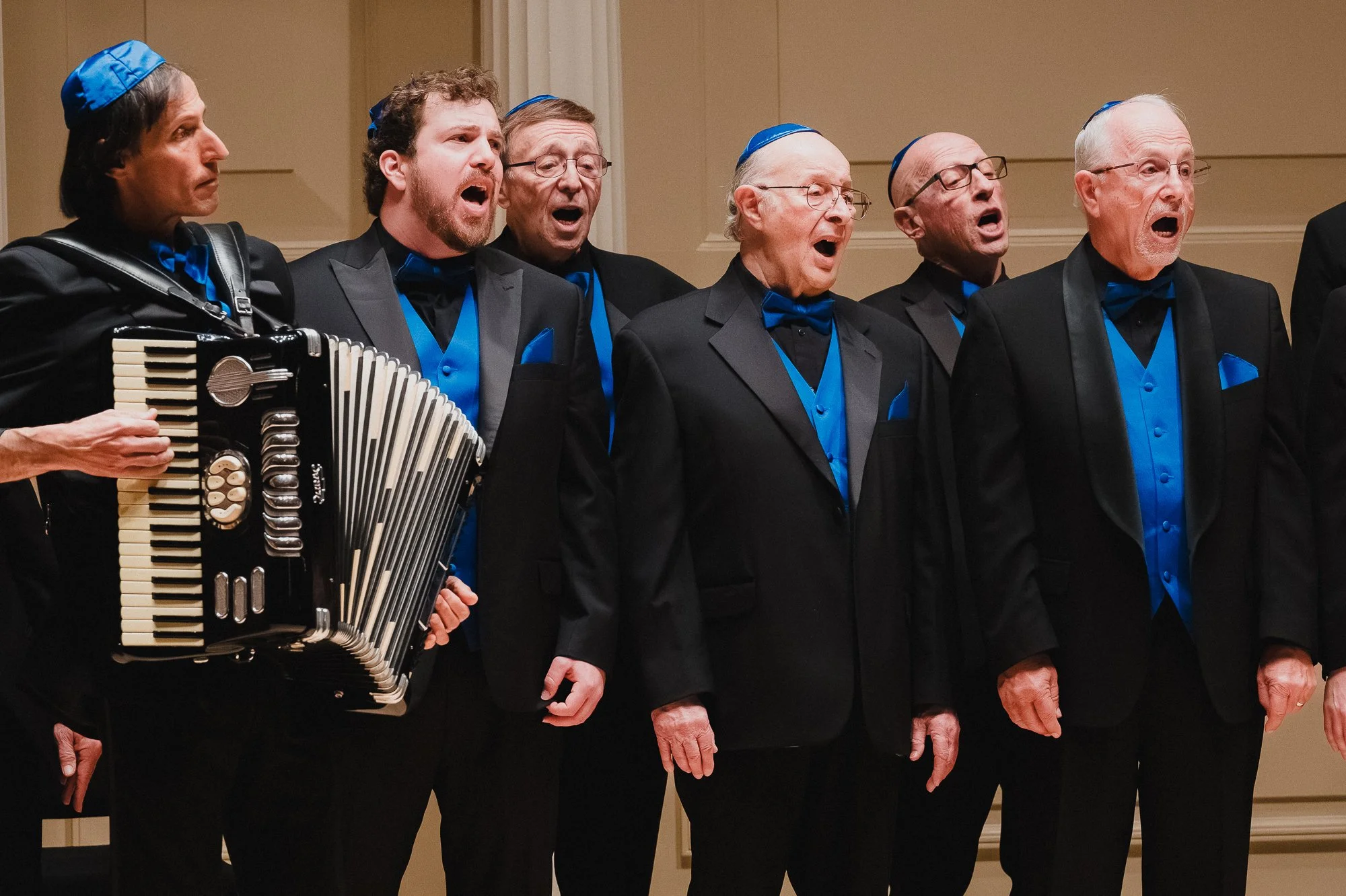 Members of the San Diego Jewish Men's Choir performing at Weill Recital Hall, Carnegie Hall, with an accordionist playing alongside them.