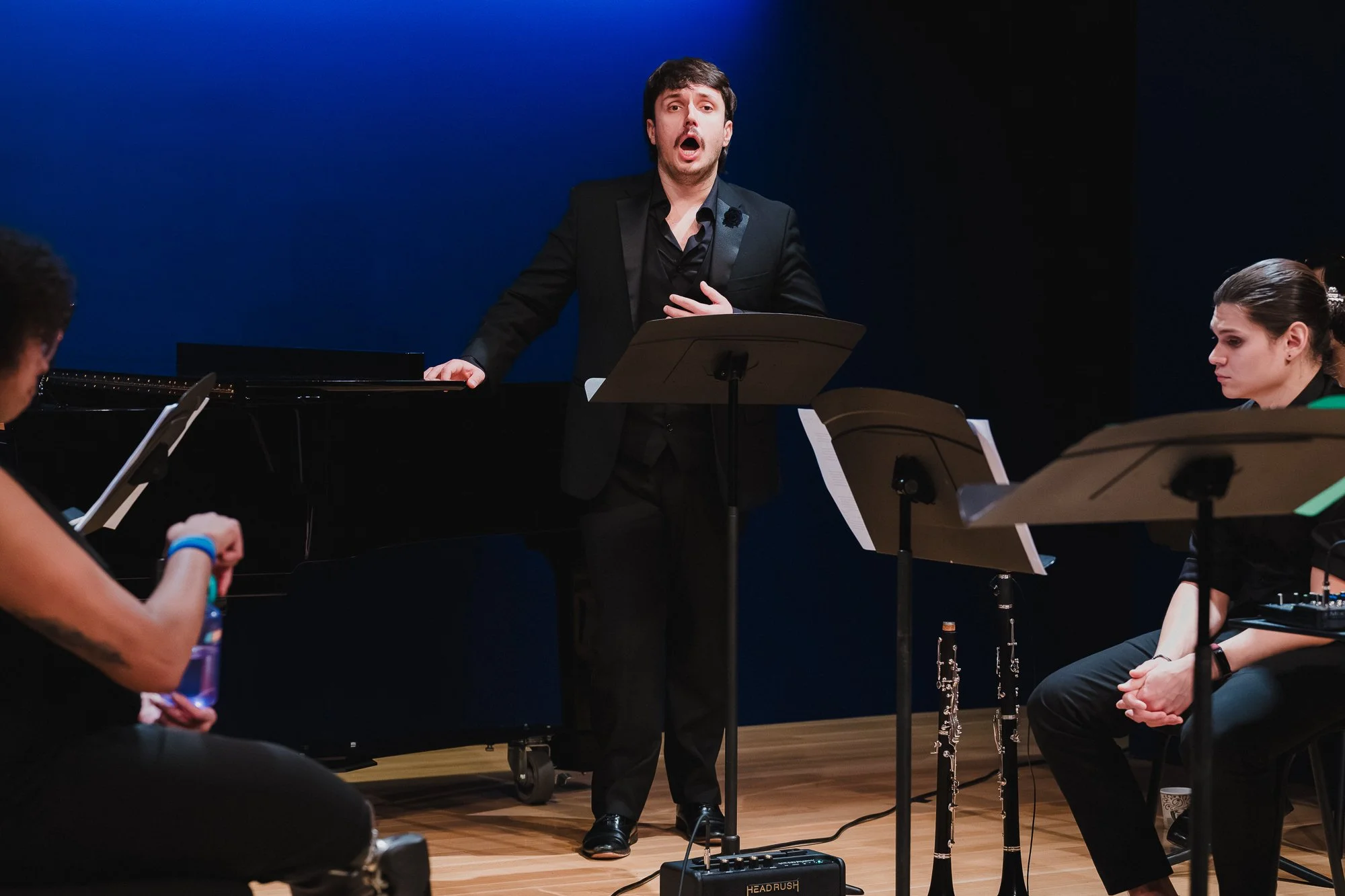 Bass-baritone Marcel Sokalski performing in black suit with hand on chest, accompanied by chamber ensemble at Marc A. Scorca Hall