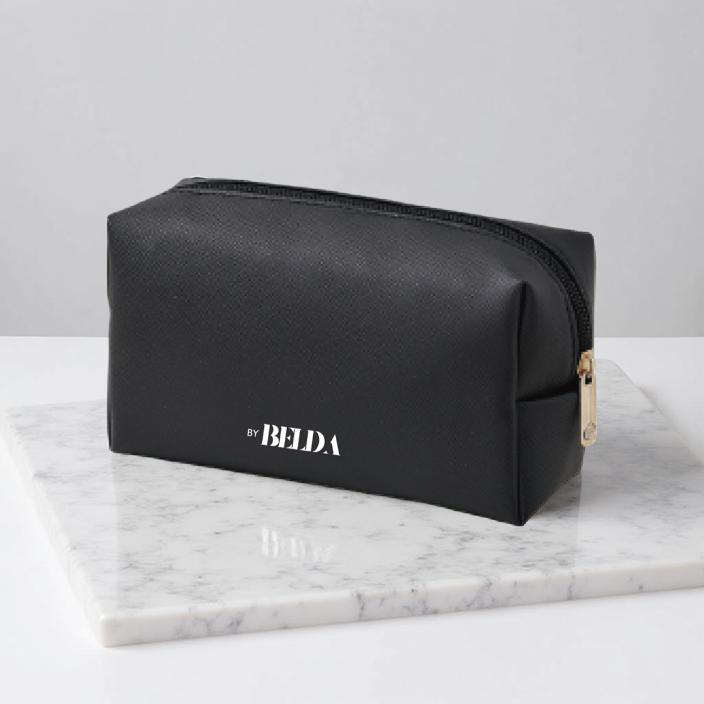 Black Belda toiletry bag with gold zipper on a white marble surface.