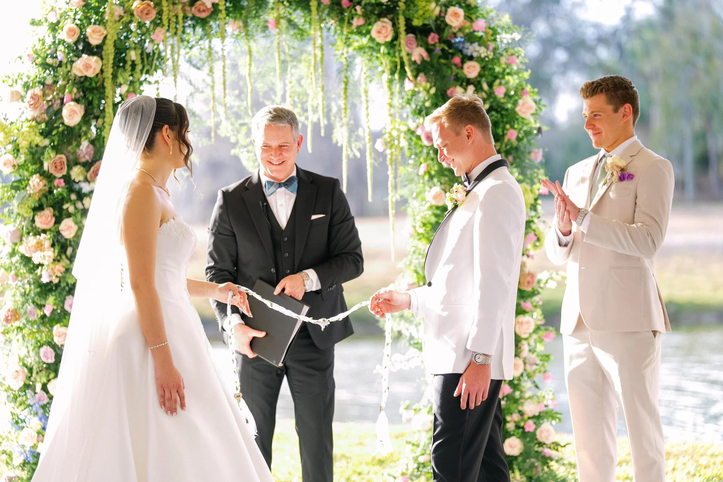 Guy Swenson of Guy Thee Wed smiling as a newly married couple reveals the tied Celtic handfasting knot with a shared smile, at their outdoor garden ceremony.
