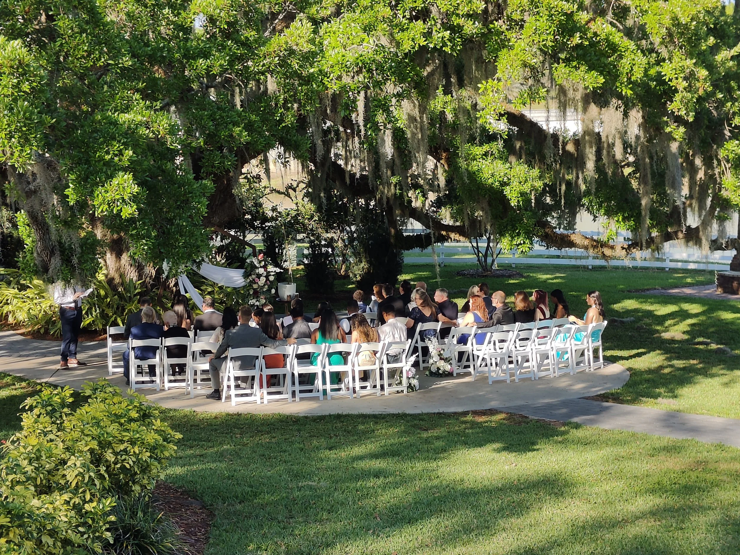 Outdoor ceremony space at the Highland Manor in Apopka Florida beneath a 100-year-old oak tree on rolling lawn with historic Victorian manor in background