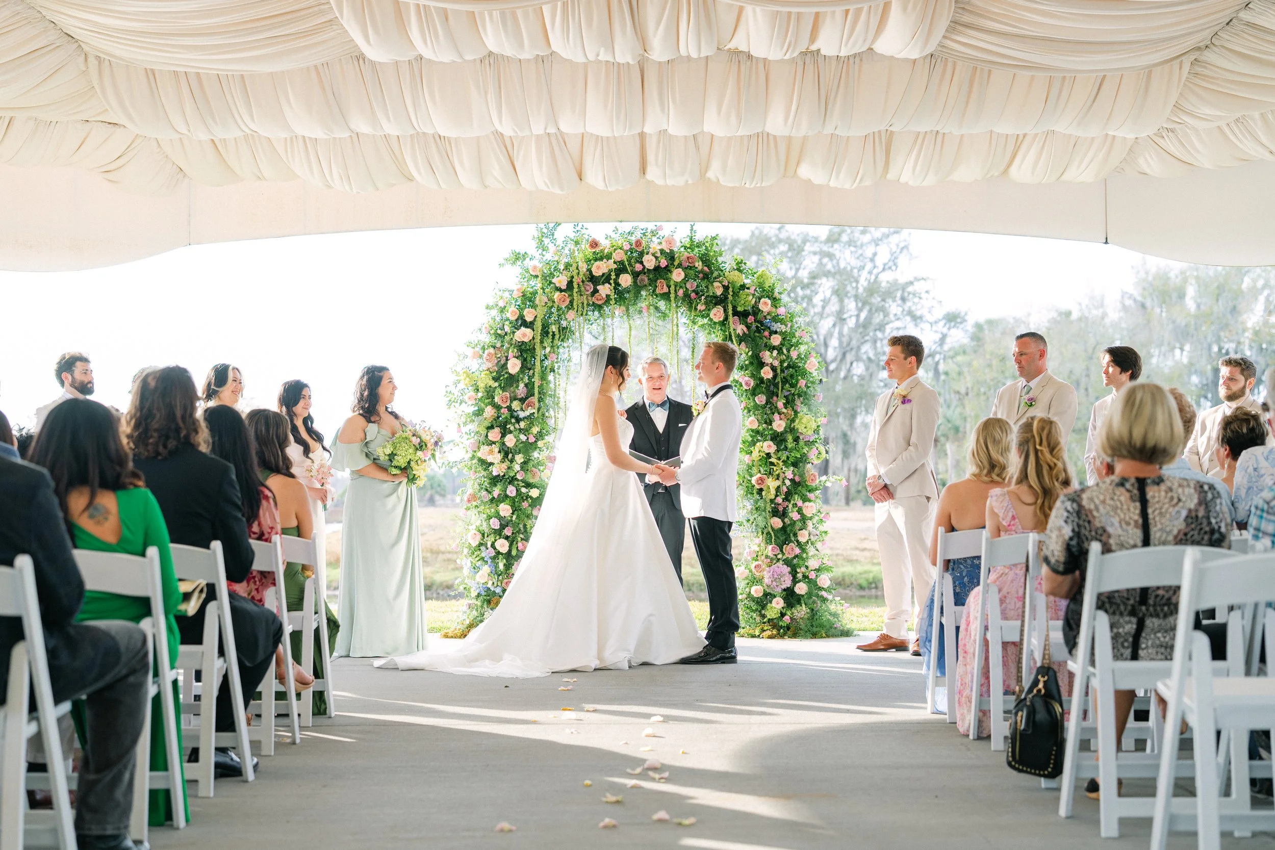 Orlando wedding officiant Guy Swenson marries a couple beneath an elegant draped canopy, in front of a lush floral arch, at a covered outdoor Central Florida wedding ceremony.