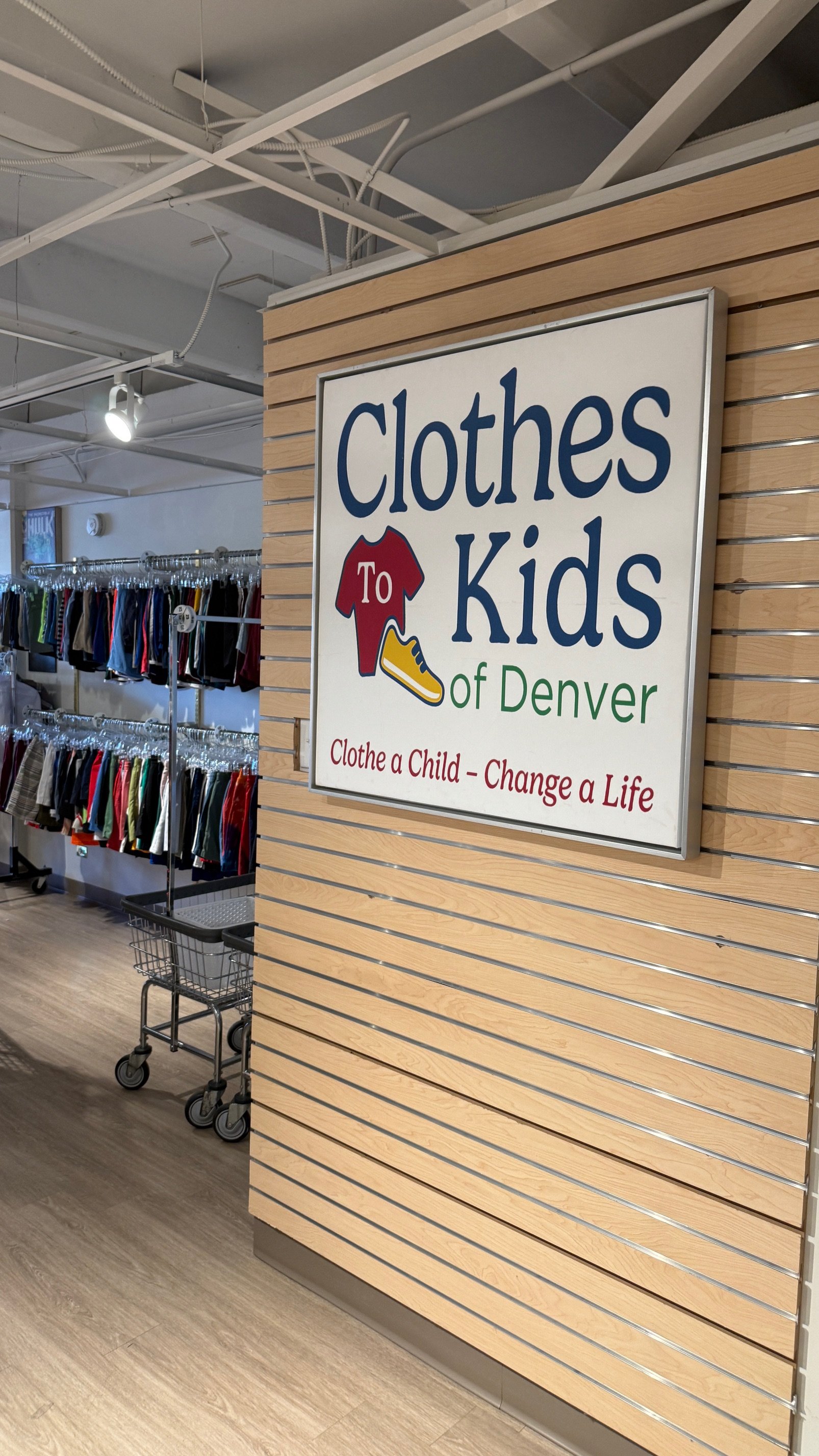 Photo of the inside of Clothes to Kids Denver with a large logo on the wall and racks of clothing on the left side background