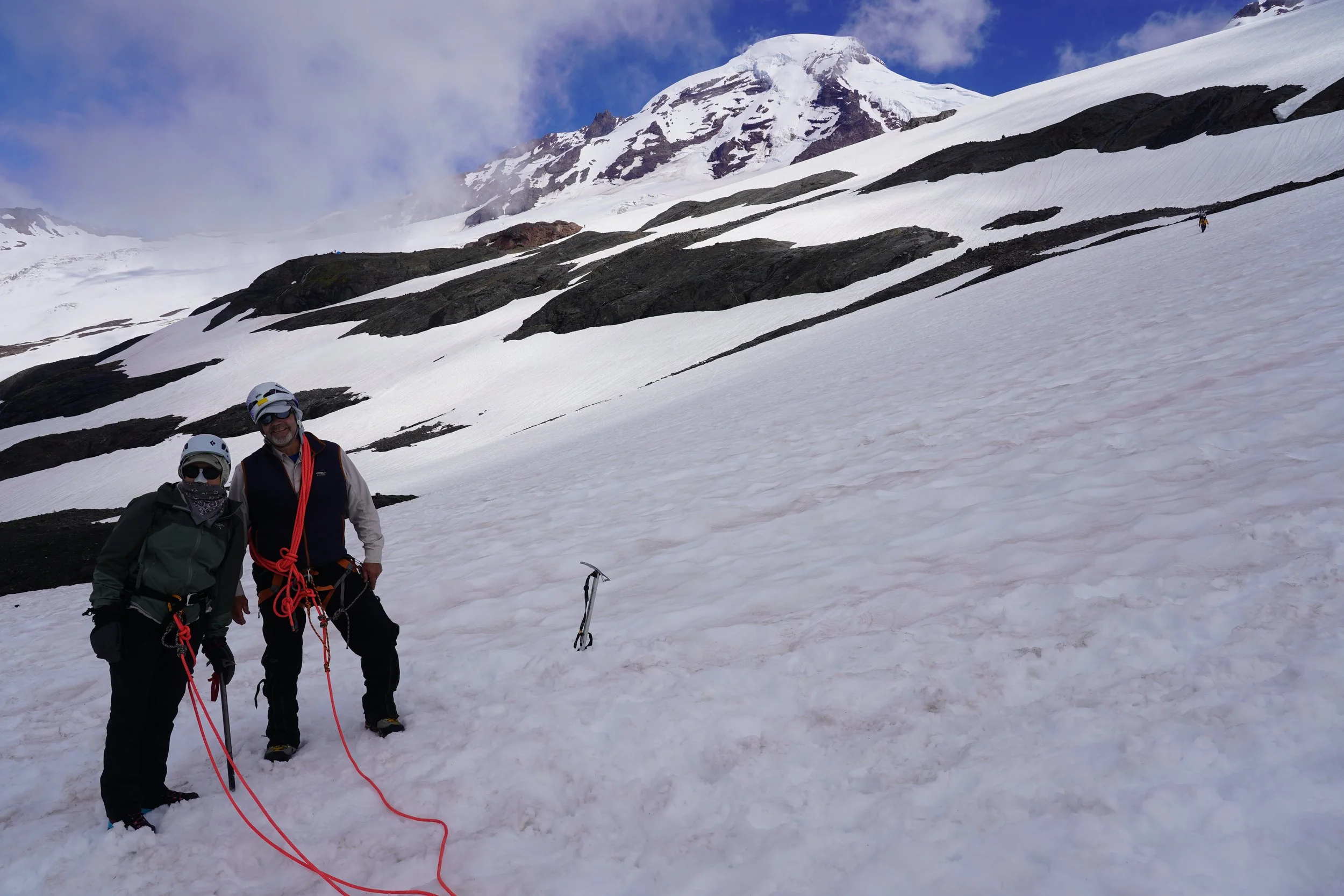 Climber helping another climber on glacier with ice axes and climbing gear