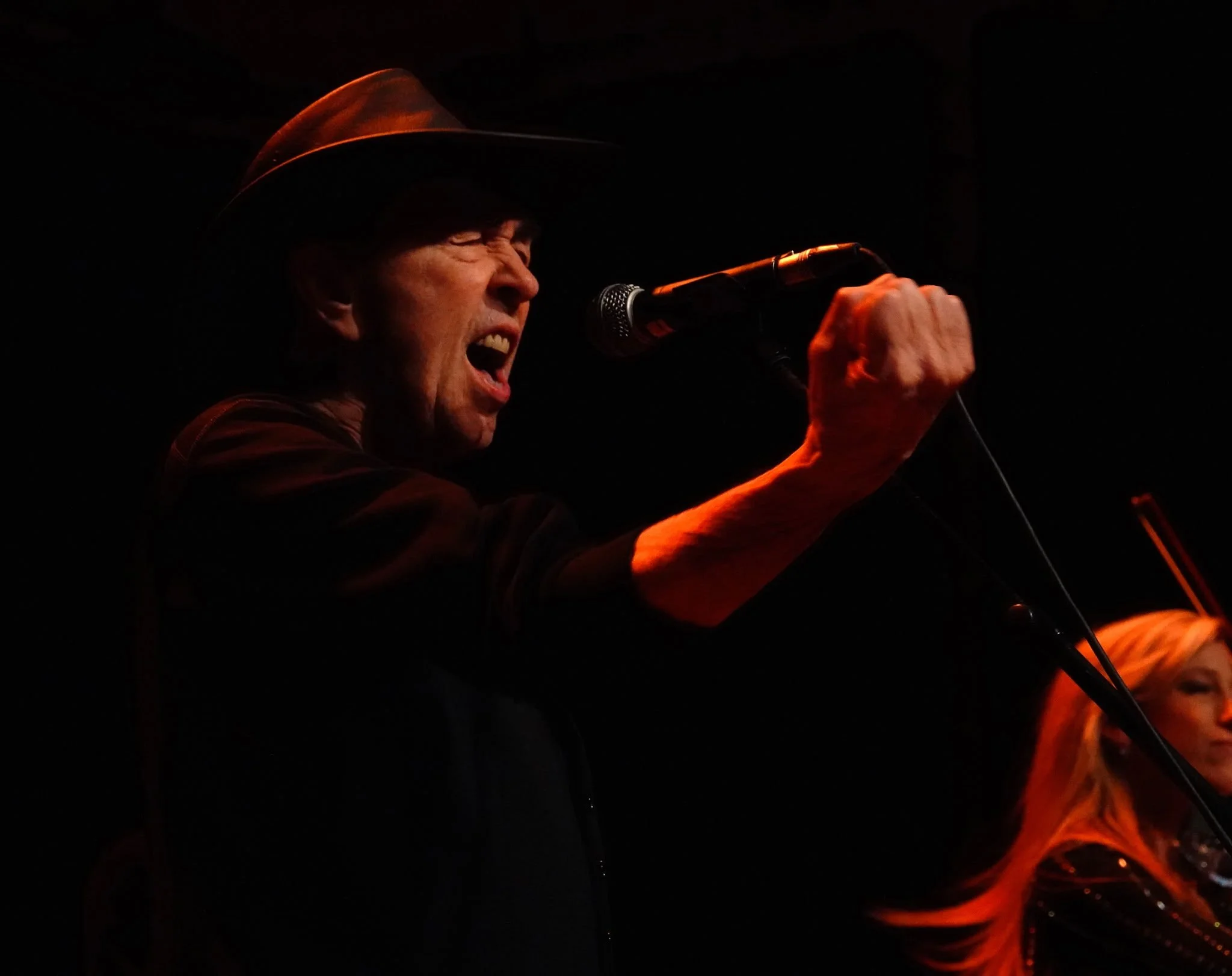 David Surkamp singing into a microphone under red stage lighting.