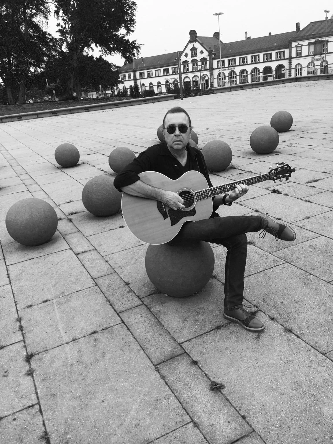David Surkamp playing acoustic guitar outdoors in a black-and-white photograph.