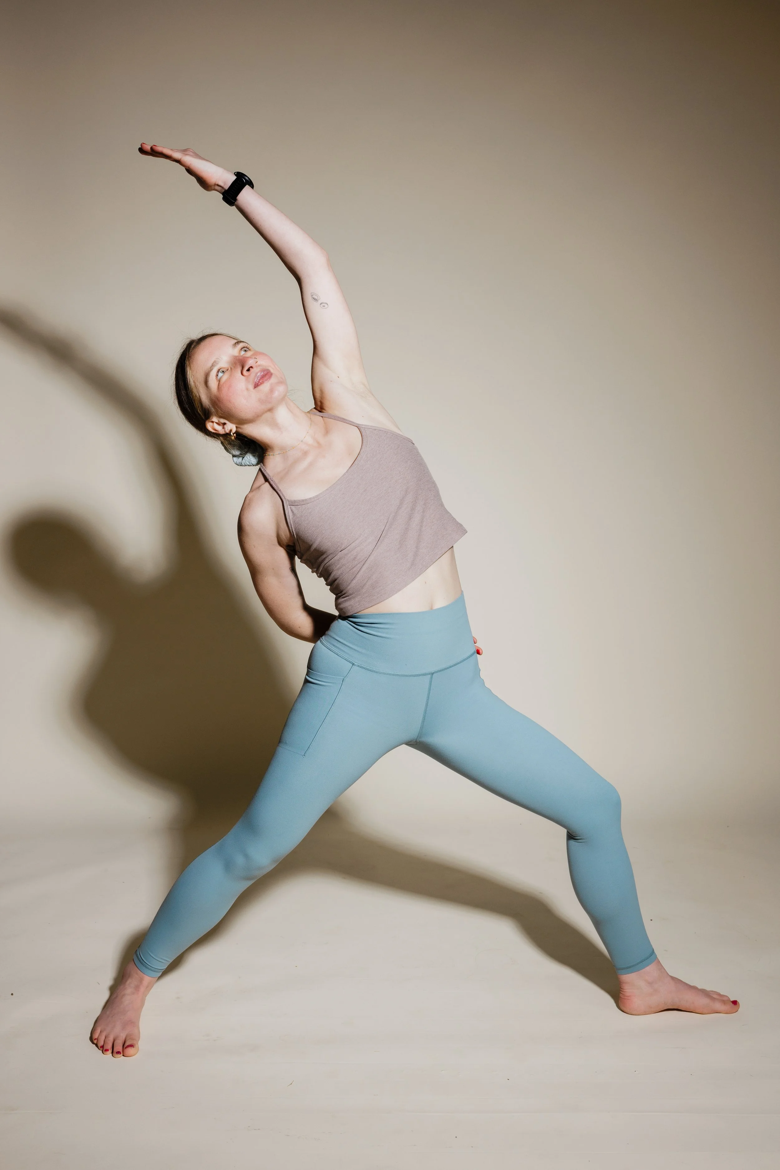 A woman doing a yoga stretch against a plain, light-colored background.