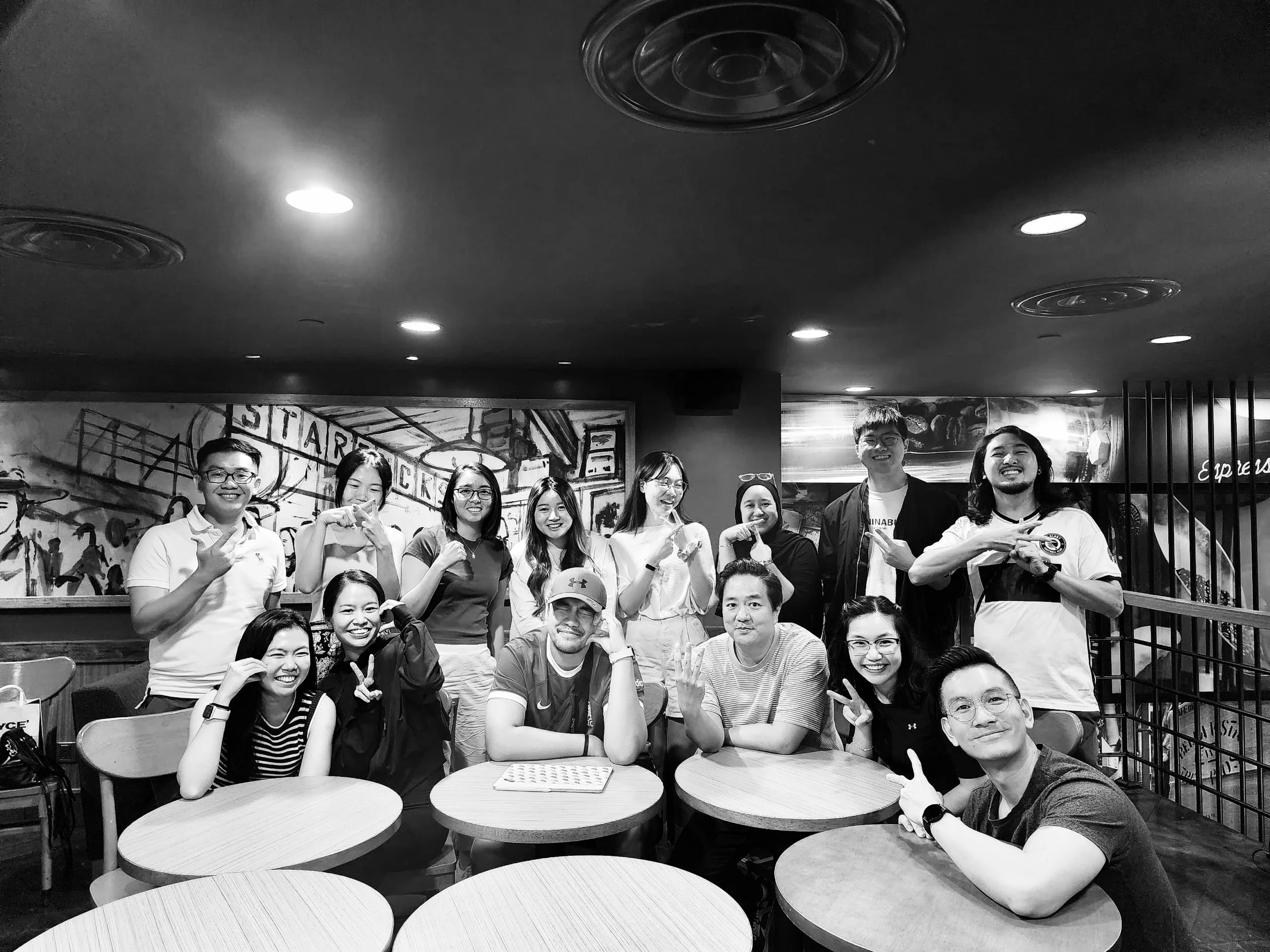 Group of people smiling and posing together in a cafe or restaurant with tables and artwork on the wall.